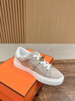 Sneaker beige in suede con suola bianca su scatola arancione e sfondo in legno.
