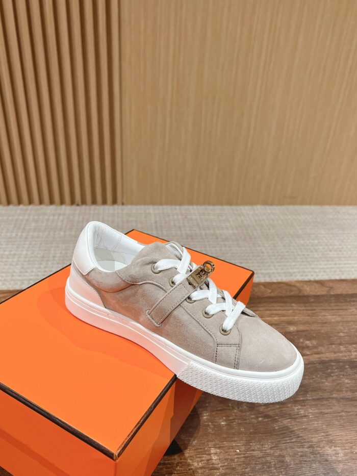 Sneaker beige in suede con suola bianca su scatola arancione e sfondo in legno.