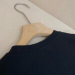 Maglia nera a girocollo su gancio in legno, stile minimal e qualità elegante.