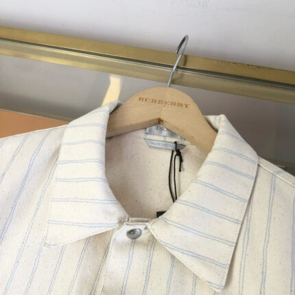 Camicia elegante a righe crema su appendiabiti di lusso, stile classico e di alta qualità.