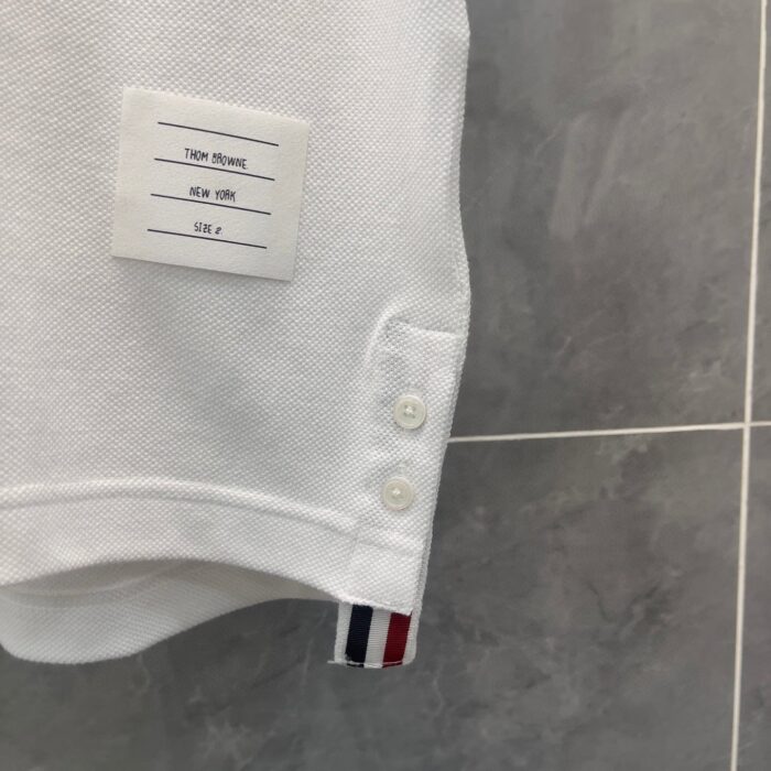 Polo bianca classica con badge a strisce rosse, bianche e blu, dettagli di qualità.