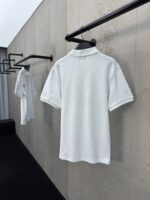 Polo bianche minimaliste su appendini neri in ambiente moderno e luminoso.