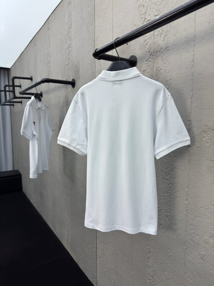 Polo bianche minimaliste su appendini neri in ambiente moderno e luminoso.