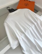 T-shirt bianca elegante, vestibilità rilassata, con sacchetto arancione di marca di lusso sullo sfondo.