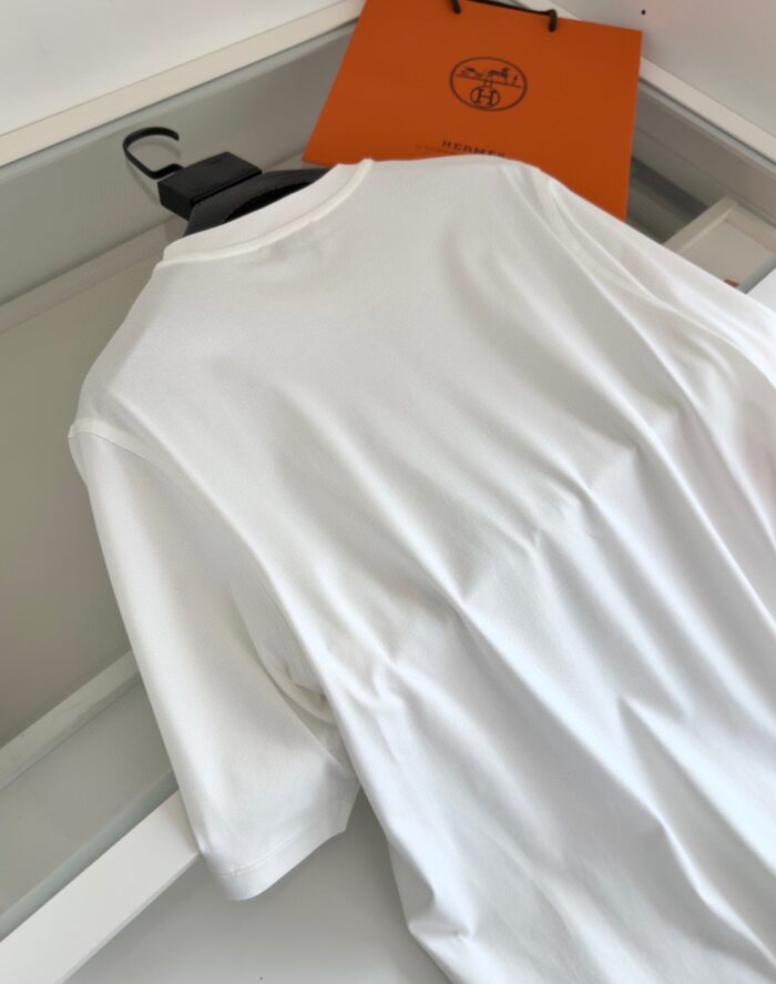 T-shirt bianca elegante, vestibilità rilassata, con sacchetto arancione di marca di lusso sullo sfondo.