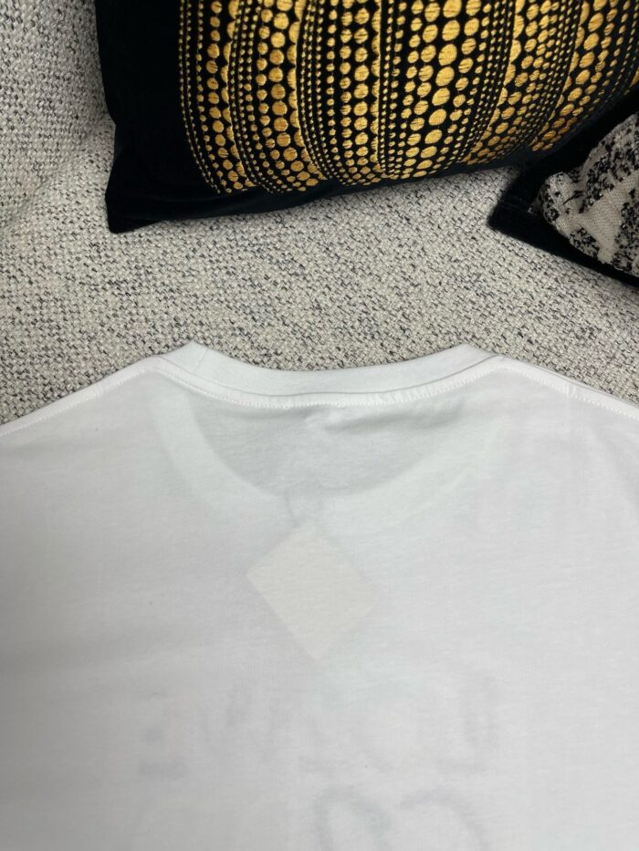 Maglietta bianca casual con tag, decorazione moderna e sfondo elegante con cuscino geometrico.