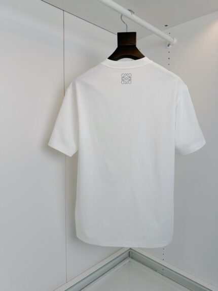 T-shirt bianca semplice, senza toppe o dettagli, su appendiabiti minimalista per look versatile.