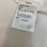 Etichetta di cura in cotone con simboli e istruzioni multilingue per lavaggio e asciugatura.