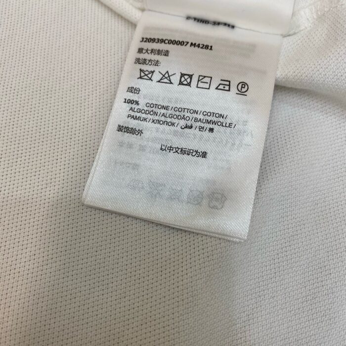 Etichetta di cura in cotone con simboli e istruzioni multilingue per lavaggio e asciugatura.