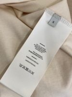 Etichetta con istruzioni di lavaggio su tessuto beige e morbido, taglia S.