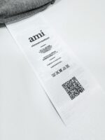 Etichetta del brand Ami con QR code e simboli di cura su tessuto grigio.