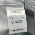 Etichetta di cura in polyester con simboli di lavaggio e dettagli di contatto.