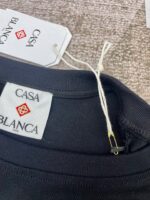 Etichetta Casa Blanca su maglietta nera, logo elegante e pin dorato, dettaglio moda sofisticata.