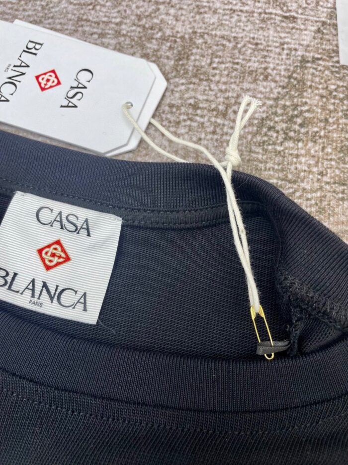 Etichetta Casa Blanca su maglietta nera, logo elegante e pin dorato, dettaglio moda sofisticata.