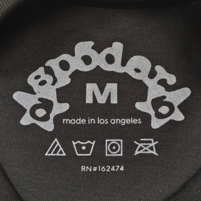 Etichetta di abbigliamento Spooder, taglia M, produzione a Los Angeles, simboli di cura.