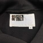 Etichetta di maglia sportiva nera con logo bianco e tag taglia M, stile urbano e trendy.