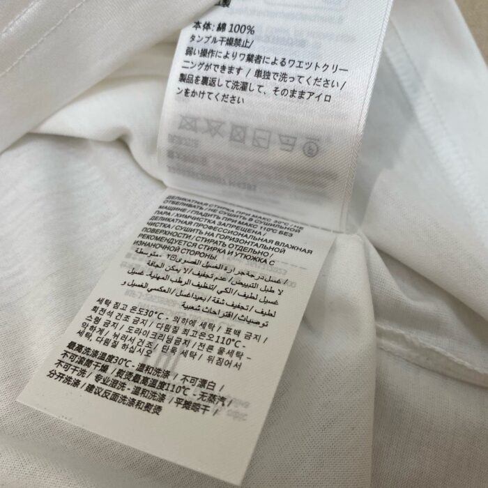 Etichetta di cura in cotone multilingue per abbigliamento, istruzioni di lavaggio e manutenzione.