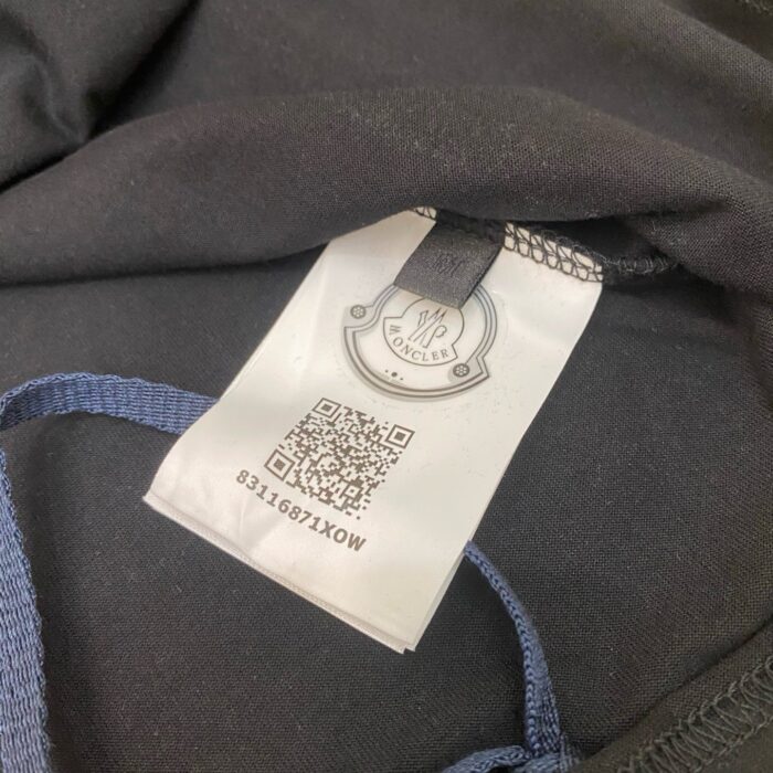 Etichetta di abbigliamento con logo, codice QR e coulisse in tessuto nero e blu.