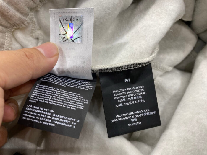 Etichette di abbigliamento con tag olografico, taglia M e origine Cina su tessuto chiaro.