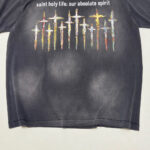 Maglietta nera con croci colorate e messaggio spirituale, stile vintage e design vibrante.
