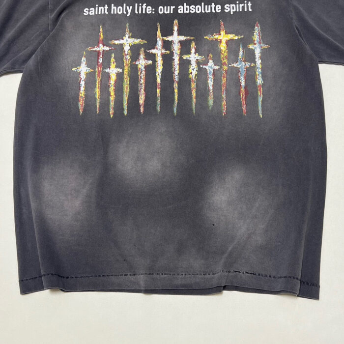 Maglietta nera con croci colorate e messaggio spirituale, stile vintage e design vibrante.