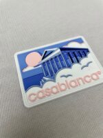 Patch artistico con colonne, sole rosa e testo “Casablanca” in stile giocoso.