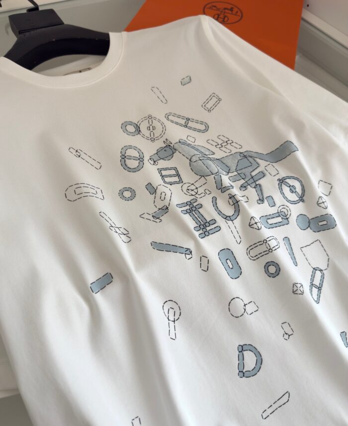 Maglietta bianca con design creativo di oggetti illustrati in blu e grigio, stile moderno e originale.