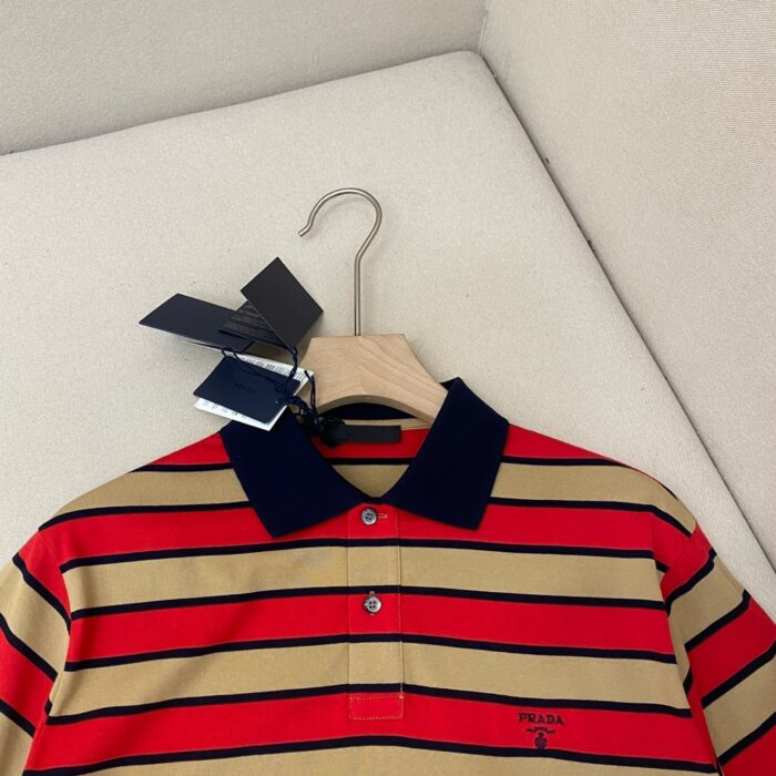 Maglietta polo a righe rosso beige con collo blu, nuova e di alta qualità su gruccia di legno.
