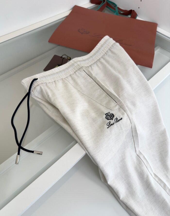 Pantaloni jogger cream con cintura nera, logo e borsa in pelle marrone, stile casual e comodo.
