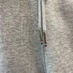 Felpa grigia con coulisse e aghetti metallici decorativi, stile casual e moderno.