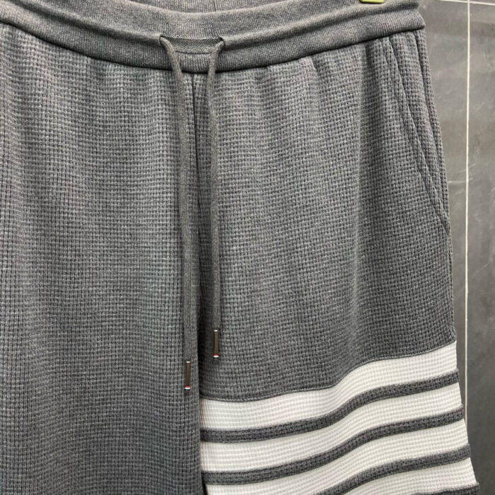 Pantaloncini felpati sportivi grigi con tasche, cinturino regolabile e dettagli a strisce bianche.