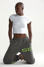 Modello urbano in posa sportiva con top crop bianco e joggers grigi con dettagli verde neon.