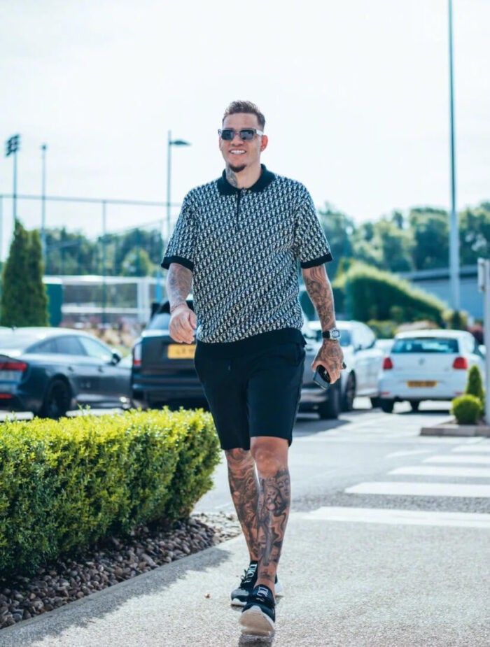 Uomo in stile casual con tatuaggi e occhiali, passeggia in area ricreativa estiva.