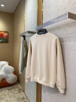 Display di moda minimalista con sweatshirt beige e verde pastello in ambiente contemporaneo.