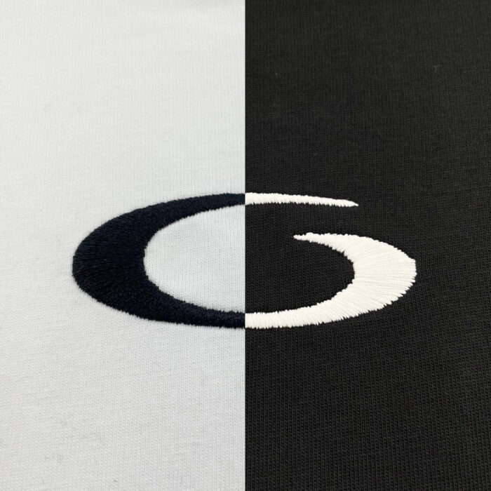 Logo ricamato bianco e nero su sfondi contrastanti, tessuti chiari e scuri, design elegante e simmetrico.