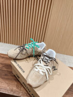 Sneakers New Balance beige con lacci verde e bianco su superficie di legno.