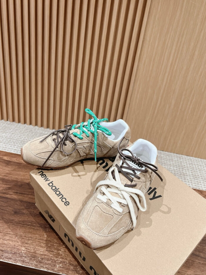 Sneakers New Balance beige con lacci verde e bianco su superficie di legno.
