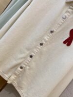 Camicia in cotone crema con bottoni metallici e ricamo rosso elegante, perfetta per ogni occasione.