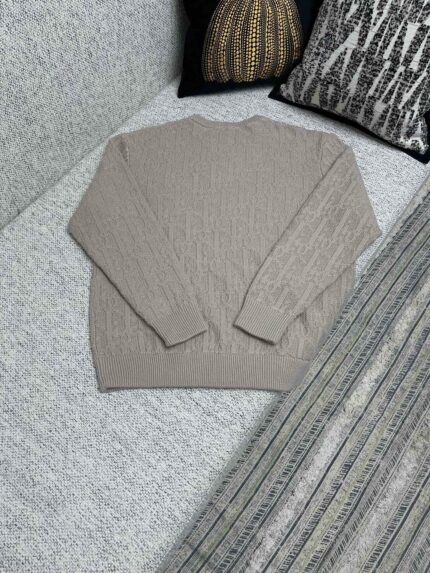 Maglione beige a treccia su divano con cuscini decorativi eleganti e accoglienti.