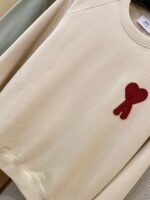 Maglione beige con fiocco rosso decorativo, stile casual e avvolgente, ideale per ogni occasione.