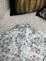 Camicia azzurra con animali e fiori, stile casual su divano con cuscini eleganti.