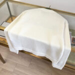 Maglione beige morbido e elegante su tavolo moderno in vetro e metallo dorato.