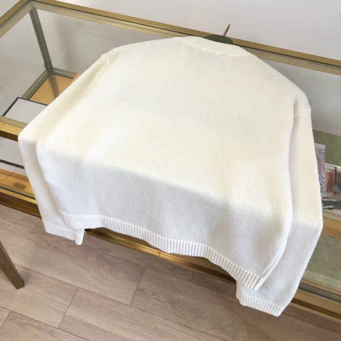 Maglione beige morbido e elegante su tavolo moderno in vetro e metallo dorato.