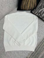 Maglione bianco casual su divano elegante con cuscini raffinati e atmosfera accogliente.