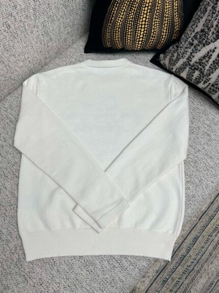 Maglione bianco casual su divano elegante con cuscini raffinati e atmosfera accogliente.