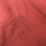 Ricamo artistico su tessuto rosso con lettera B stilizzata, eleganza e stile fatto a mano.