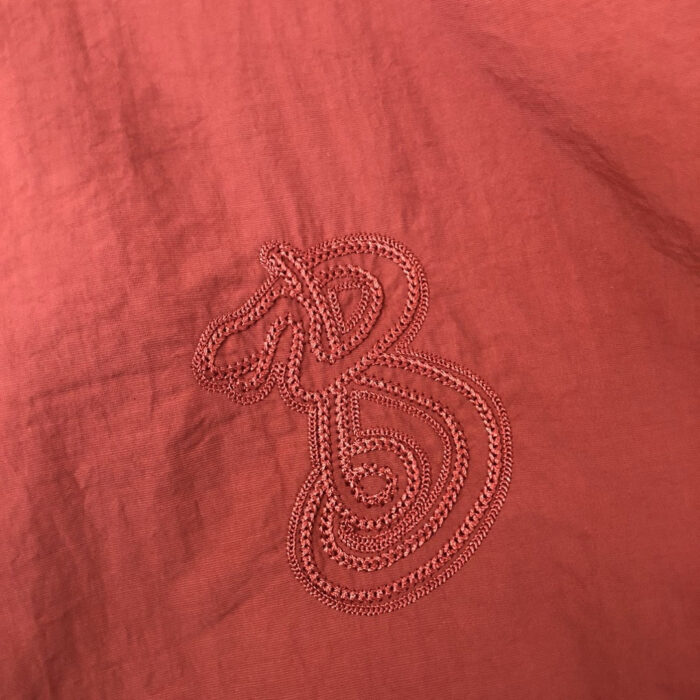 Ricamo artistico su tessuto rosso con lettera B stilizzata, eleganza e stile fatto a mano.