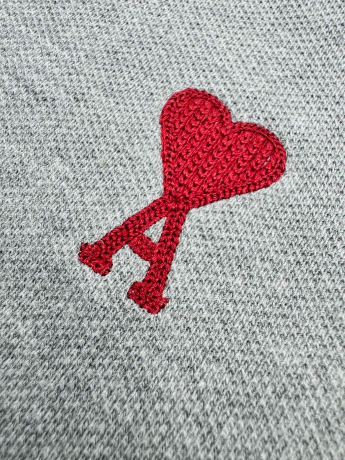 Ricamo a cuore rosso con lettera A su tessuto grigio caldo e morbido.