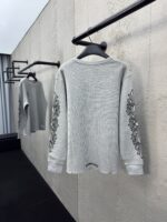 Maglione grigio elegante con ricami floreali, su asta minimalista in ambiente industriale moderno.