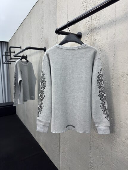 Maglione grigio elegante con ricami floreali, su asta minimalista in ambiente industriale moderno.